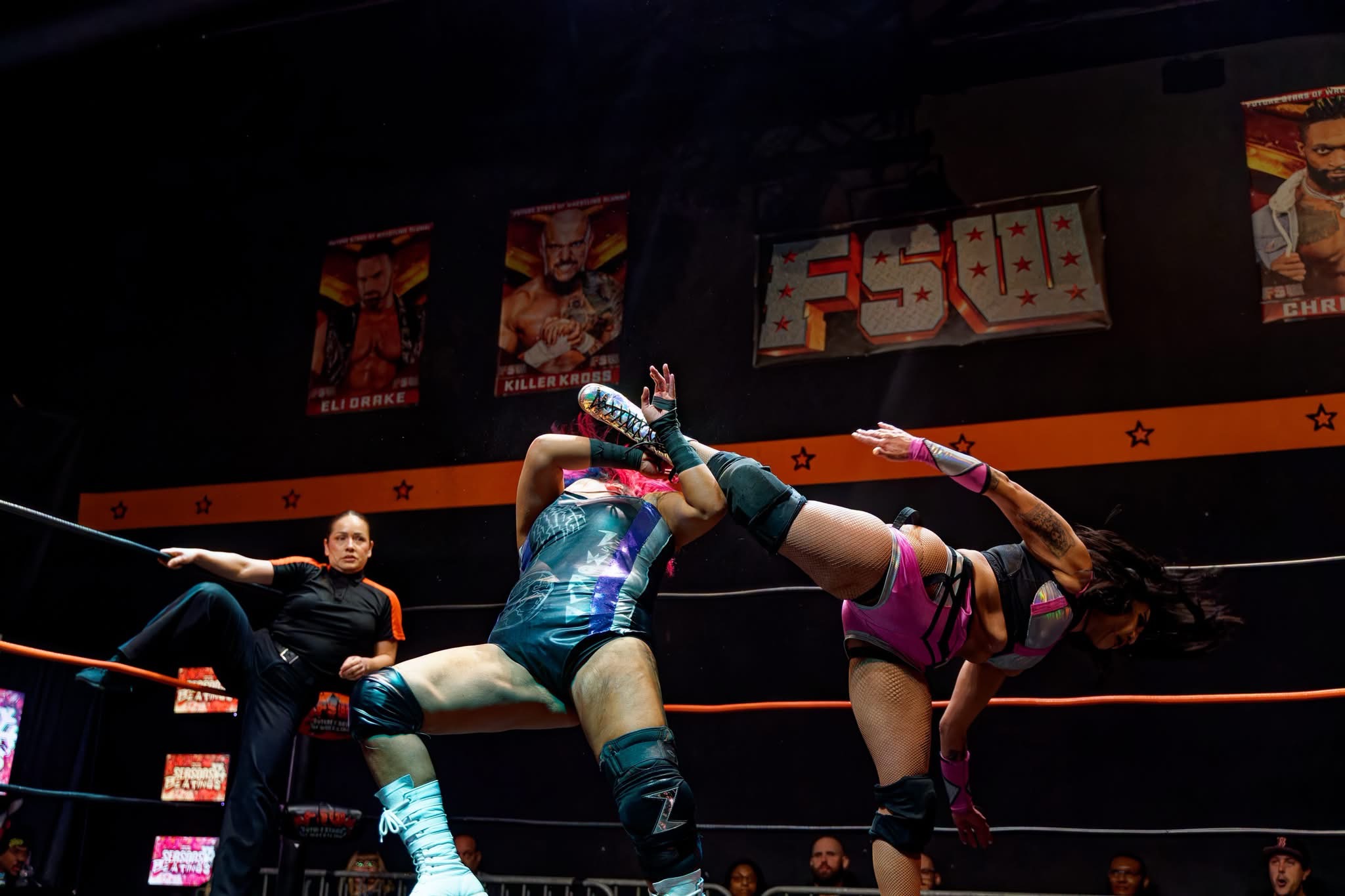 Gypsy Mac in pink gear landing a high kick to an opponent's head in an FSW ring as the referee looks on